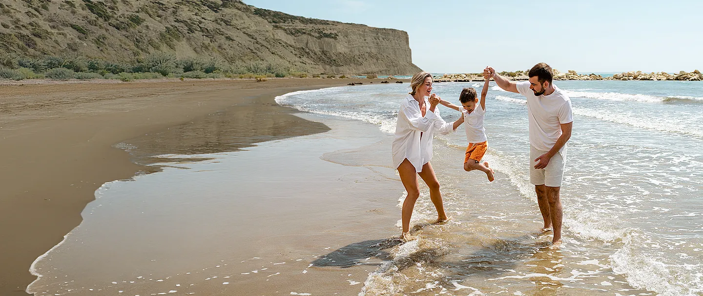 Eine glückliche Familie genießt einen spielerischen Spaziergang an einem Mittelmeerstrand.